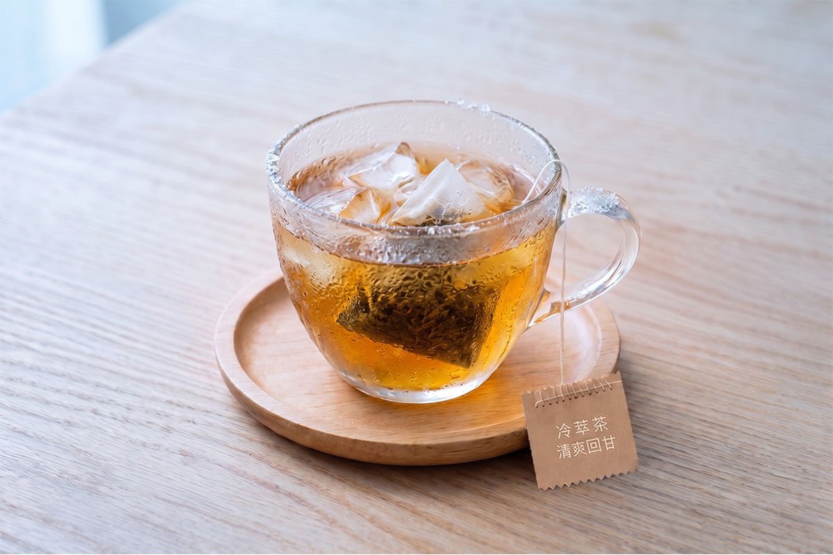 OriaTea cotton-stitched tea bag cold brewing in iced glass cup, plastic-free and glue-free for 24-hour safe cold steeping