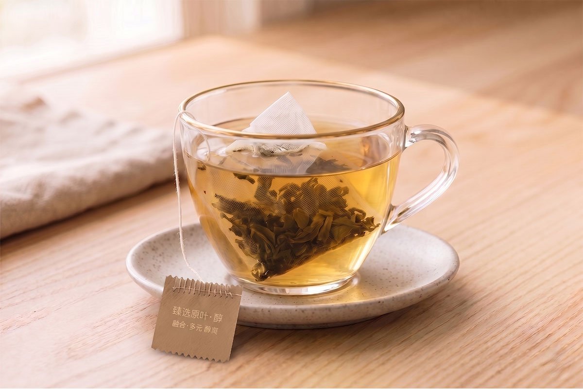 OriaTea cotton-stitched tea bag brewing whole-leaf green tea in glass cup